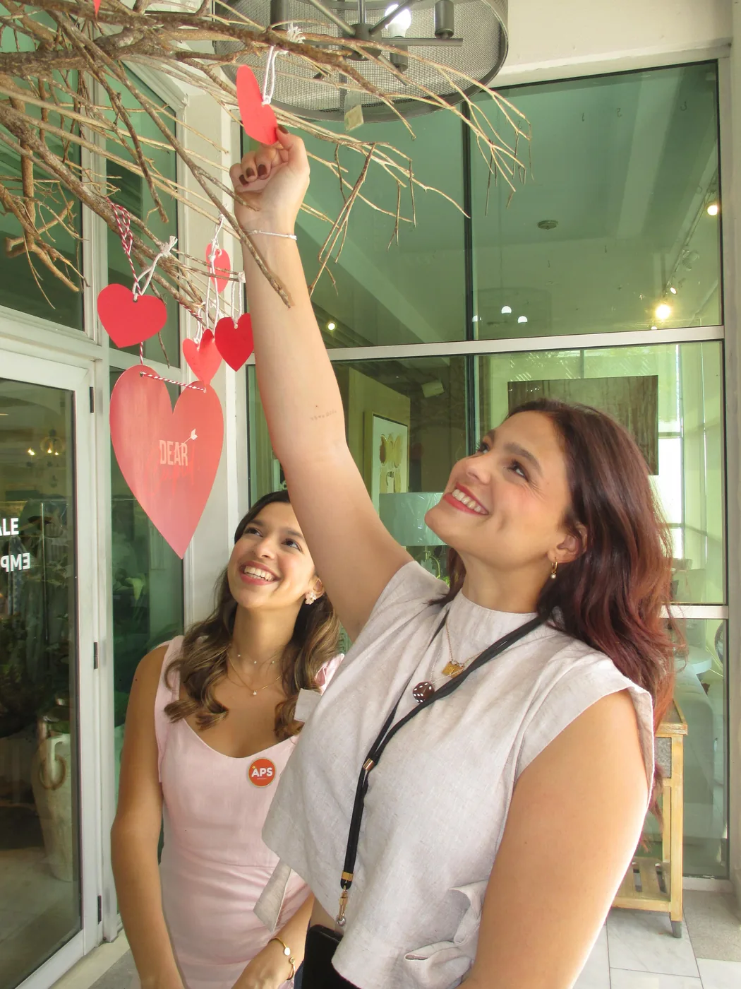 Dos voluntarias colgando corazones de papel en la decoración del bazar