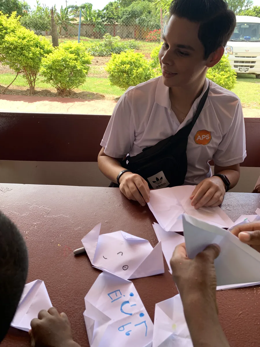 Un voluntario hace origami junto a un niño en una mesa