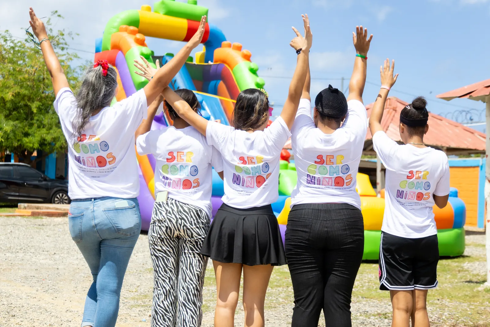 Voluntarias de espaldas con las camisetas “Ser como niños”, con los brazos en alto