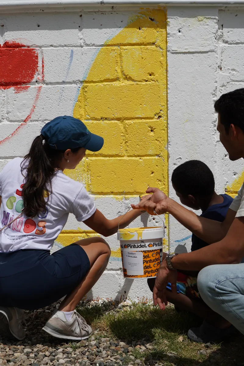 Voluntaria pasando una cubeta de pintura durante el mural
